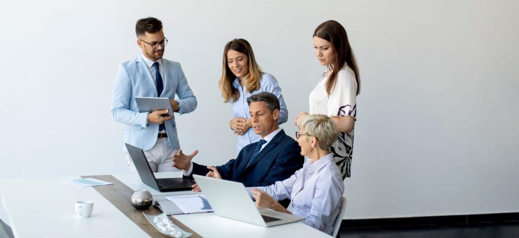 Five people around laptops listening to one speaker