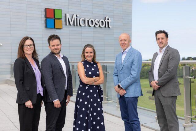 Five people stood outside a large building with a sign that says 'Microsoft' on the building.