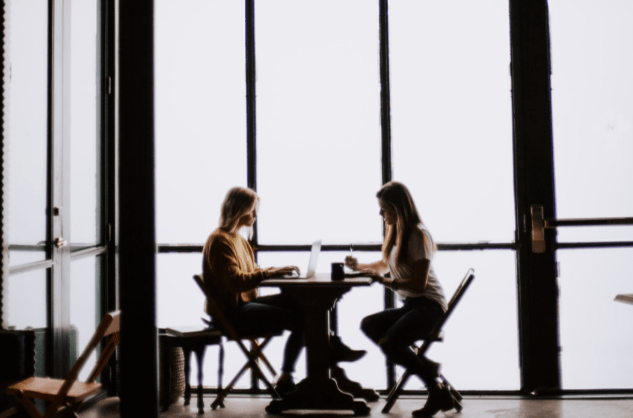 Two women sat opposite each other at a table with laptops