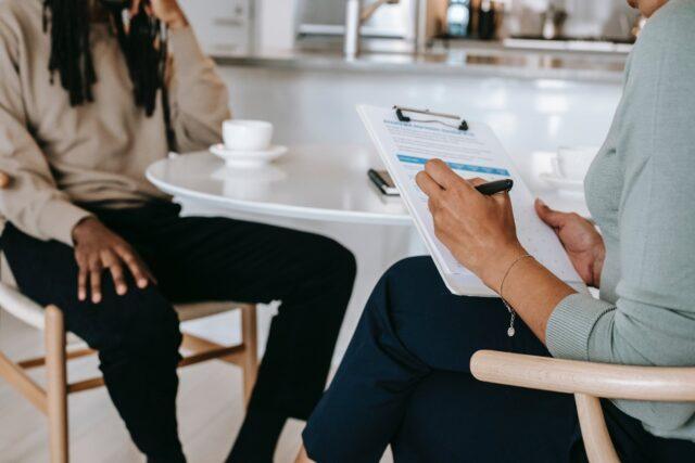 Close up of a person using a clipboard when speaking with another person at a coffee table