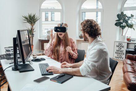 2 people working at a desk, one person wearing a VR headset