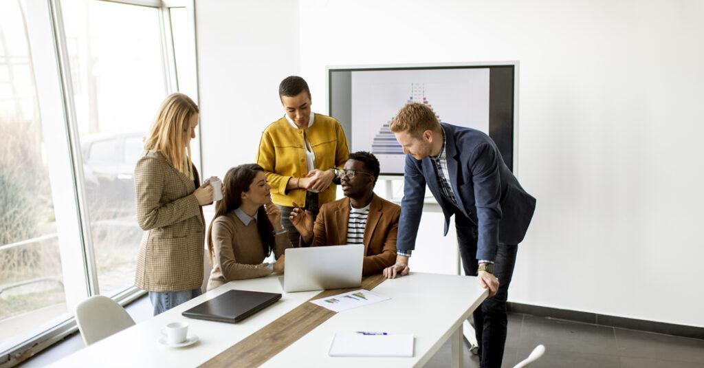 group of five business individuals gathered around a laptop